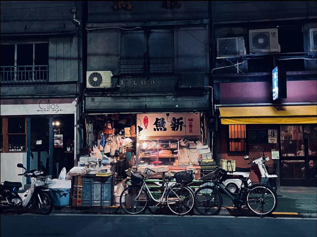 Night photograph of bicycles parked outside a three-generation family fish shop in Tokyo, red sign lit above the counter