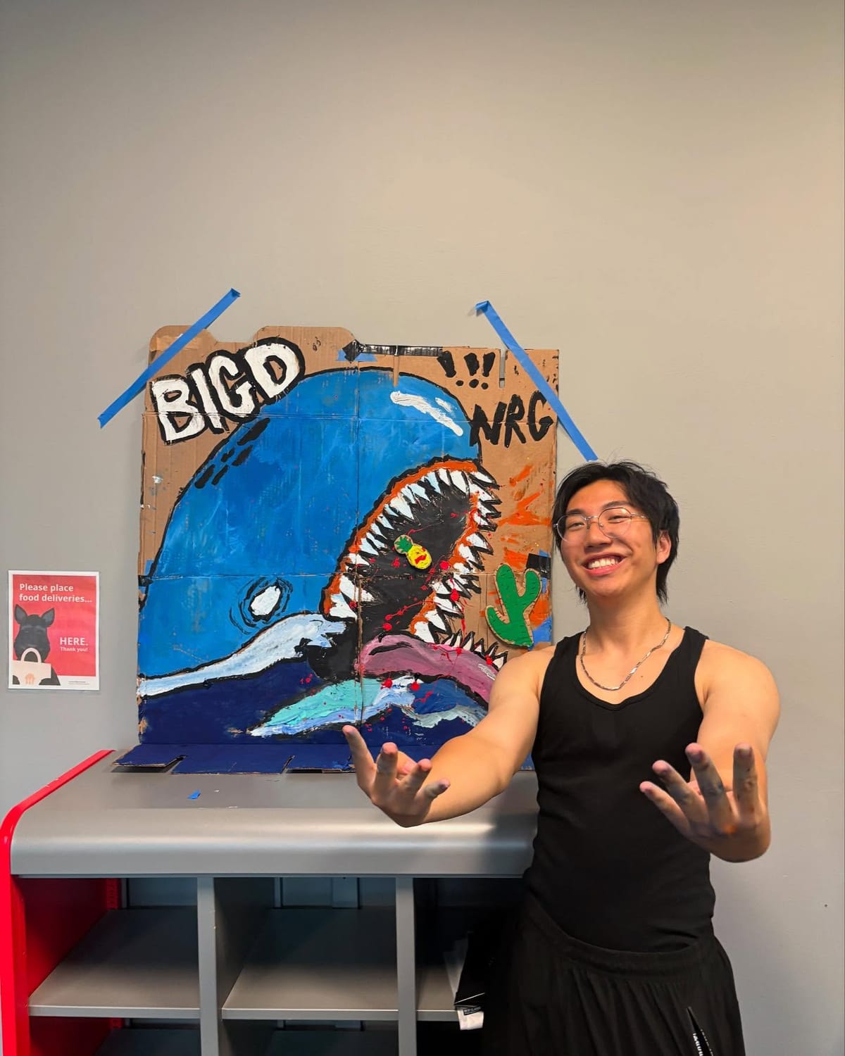 Eric Torii holding up an acrylic-on-cardboard painting of a blue whale reading “BIG D NRG”, the Donner dorm mascot sign at CMU