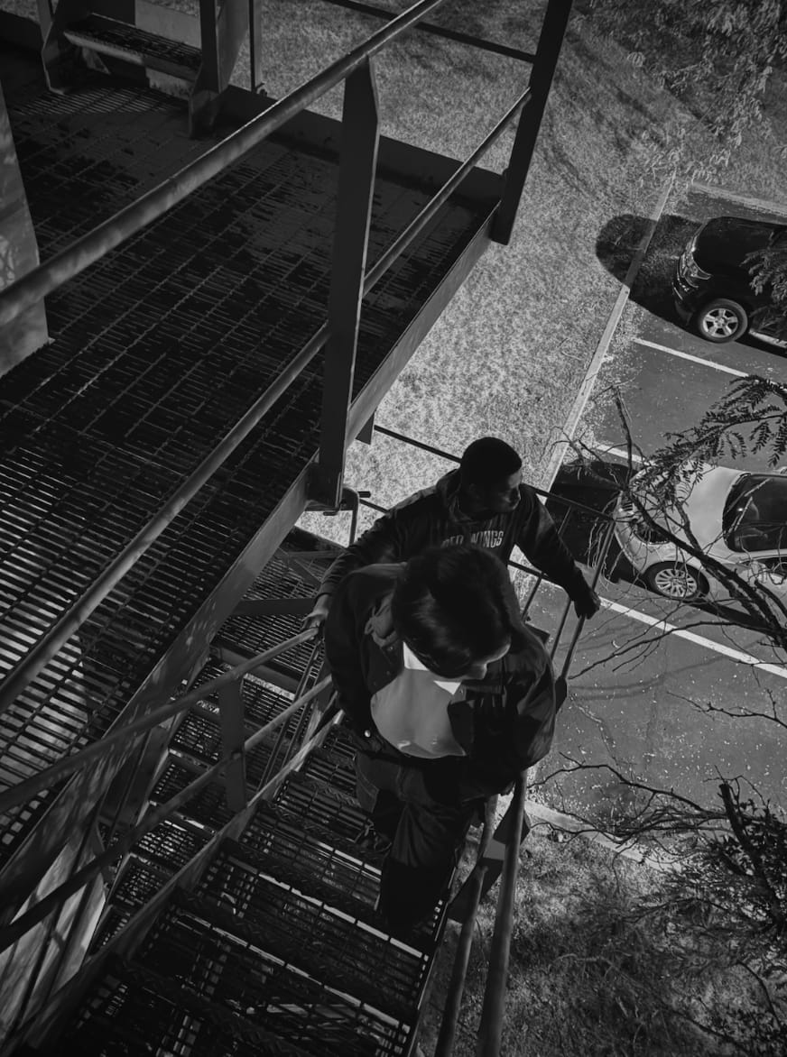 Black-and-white photograph looking down a metal stairway at two friends, Perry Chen and Ray Oji, on an abandoned structure